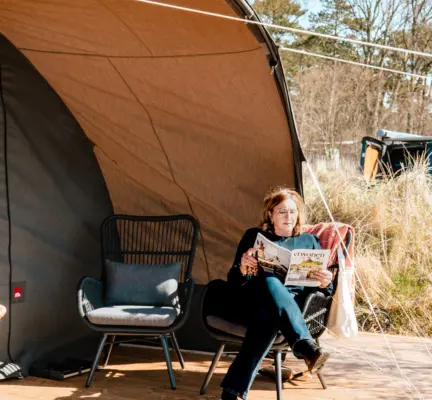 glamping in de dune tent deluxe vrouw zit in stoel en leest op het terras