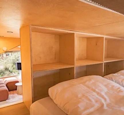 tweepersoonsbed op de vide van de tiny timber met glazen raam in dak om sterren te kijken